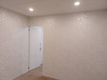 Minimalist room with textured beige walls, wooden floor, and a partially open white door.
