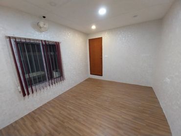 Empty room with wooden floor, white walls, window with vertical blinds, and a closed wooden door.