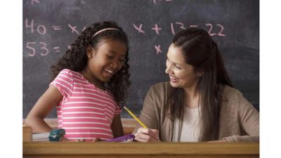 Teacher helping a young girl with math homework in class.