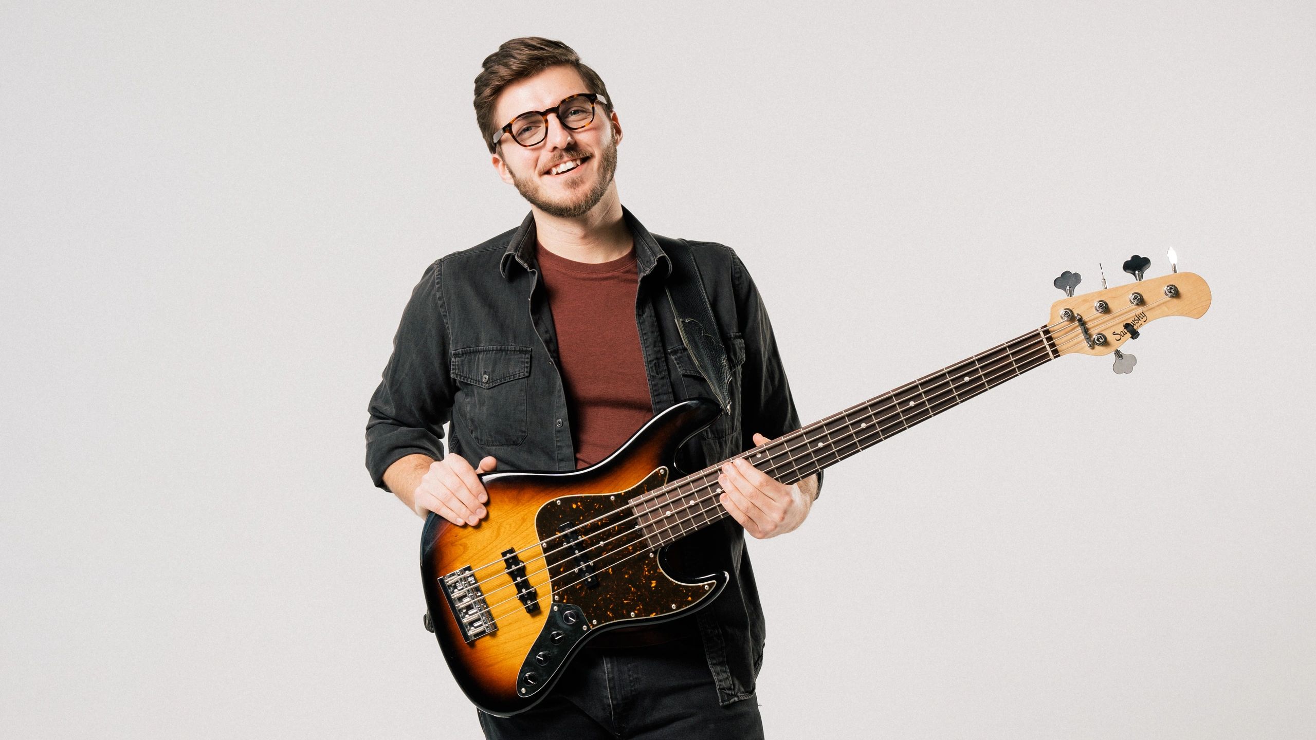 Smiling musician holding electric bass guitar. Photo credit: Skinny