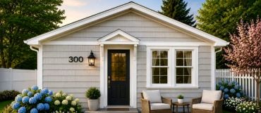 Cozy gray house entrance with black door and outdoor seating.