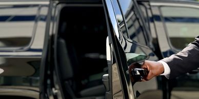 A person in a suit opening a black vehicle door.