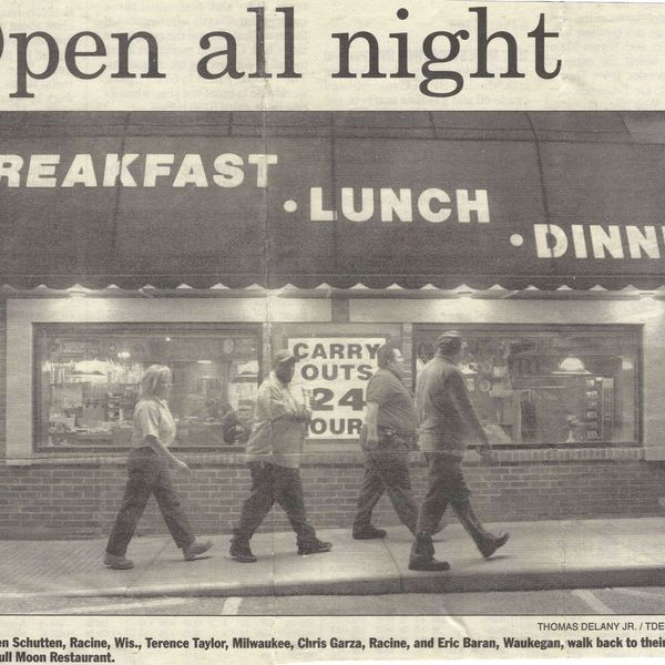 Four men walk past a 24-hour diner at night.