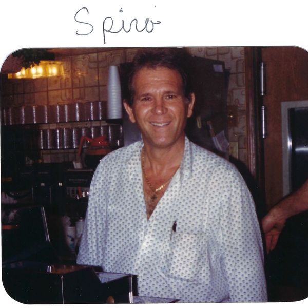 Smiling man in a patterned shirt behind a counter in a cozy setting.