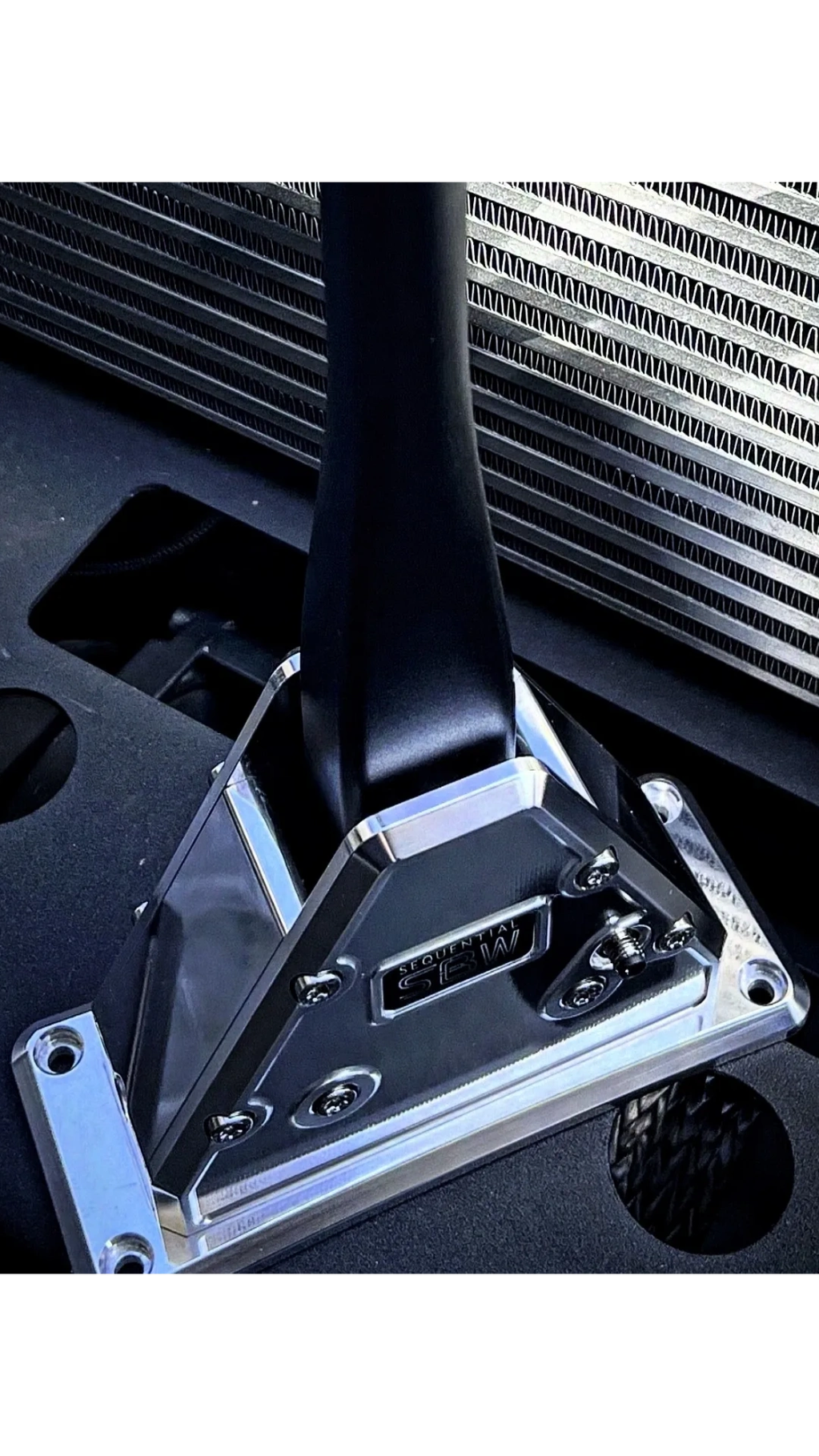 Close-up of a sequential gear shifter in a car with an intercooler in the background.