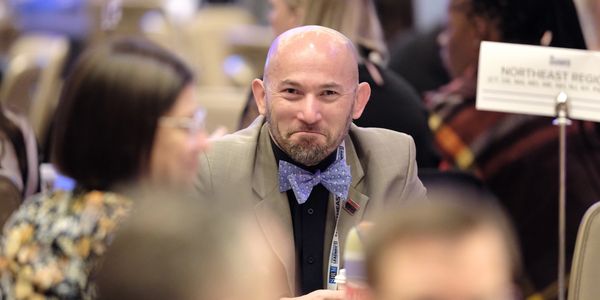 Tom Schin, smirking while sitting at a table, wearing a bright star fish bowtie.