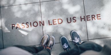 two sets of feet next to sign on sidewalk reading "passion led us here"