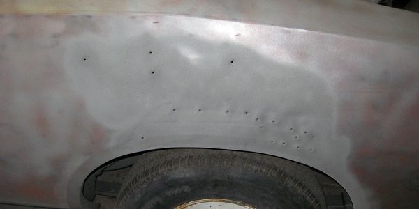Car door with dents and holes above the wheel.