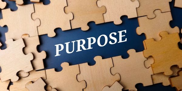 Wooden puzzle pieces surrounding the word 'PURPOSE' on a dark background.