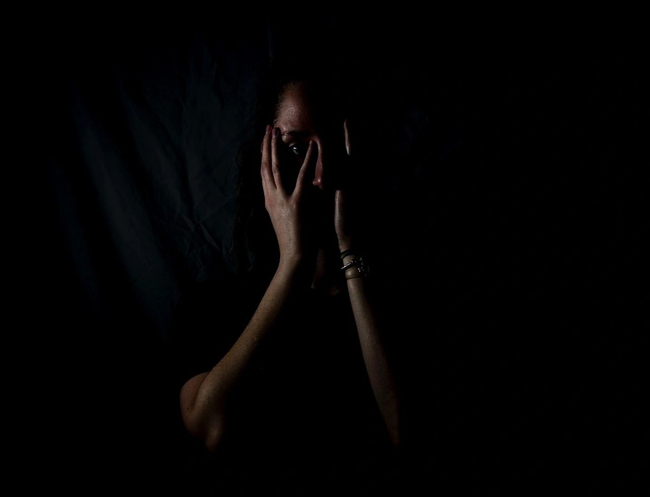 A person in the dark with their hands over their face. A person in the dark with their hands over their face.
