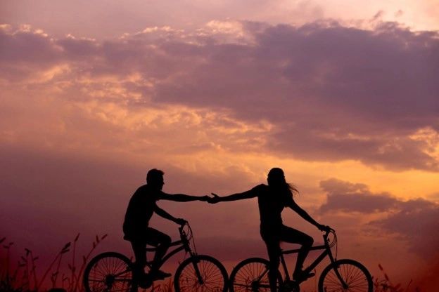 A couple riding bikes and holding hands while the sun is setting. A couple riding bikes and holding hands while the sun is setting.