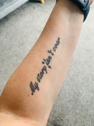 Tattoo on arm saying 'My story is not over'