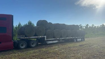 Red semi hauling round hay bales on a step deck trailer, agricultural freight, Panama City, FL