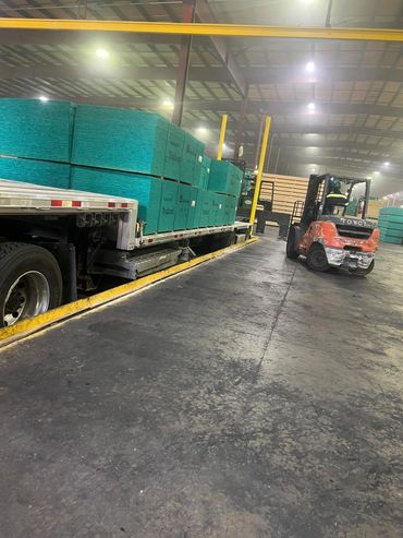 Forklift loading wrapped lumber bundles onto a flatbed trailer inside a warehouse, Panama City, FL