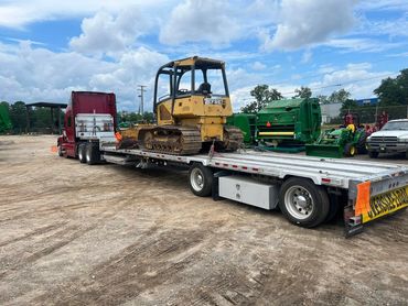 Yellow bulldozer and green farm equipment on a step deck with oversize flags, Panama City, FL