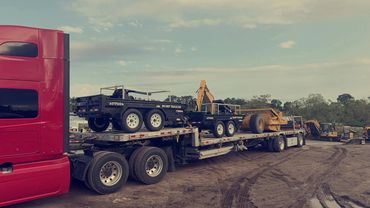 Red semi with a step deck loaded with utility trailers and construction equipment, Panama City, FL