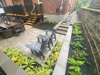 Cozy backyard patio with seating and lush greenery along stone pathways.