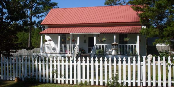 a house with a porch, red roof, and white picket fence