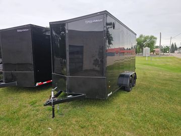 Black enclosed trailer parked on grass with another trailer nearby.