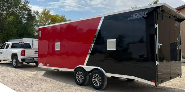 A white GMC truck towing a red and black Revy Limited trailer on a gravel surface.