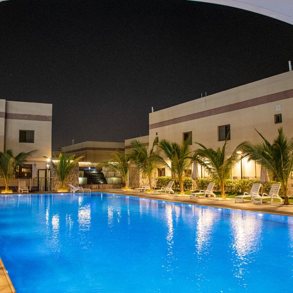 A well-lit outdoor swimming pool at night with lounge chairs and palm trees.