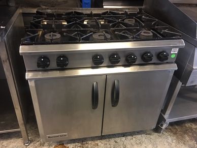 Industrial stainless steel gas stove with six burners and dual oven doors.