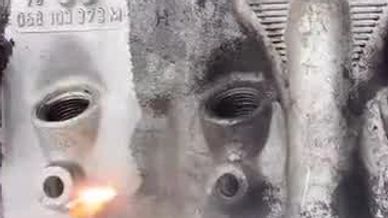 A metal engine part being cleaned with a flame torch against a mesh background.