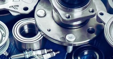 Various metallic automotive parts including spark plugs and bearings on a blue wooden surface.