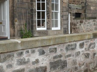 Stone houses with a stone wall and paved sidewalk on a cloudy day.