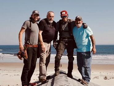 Four men standing on a rooftop by the beach, smiling and posing together.