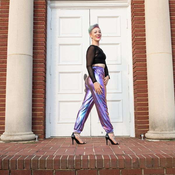 Woman in shiny purple pants and black heels walking outside.