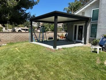 Modern black patio cover over a concrete slab in a backyard.