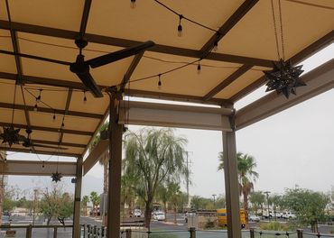 Covered outdoor seating area with ceiling fans and hanging lights overlooking a parking lot.