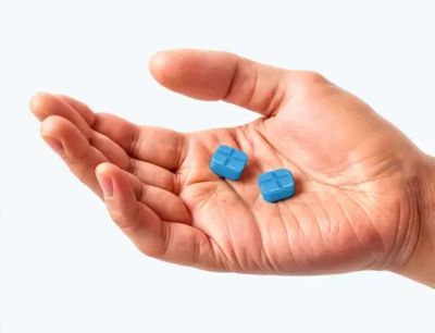 Hand holding two blue pills.
