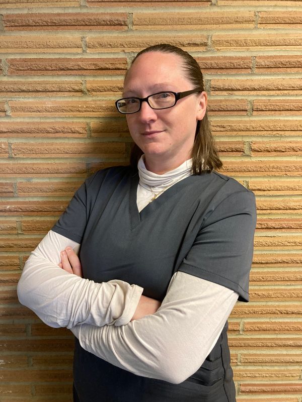 Woman in scrubs standing confidently with arms crossed against a brick wall.