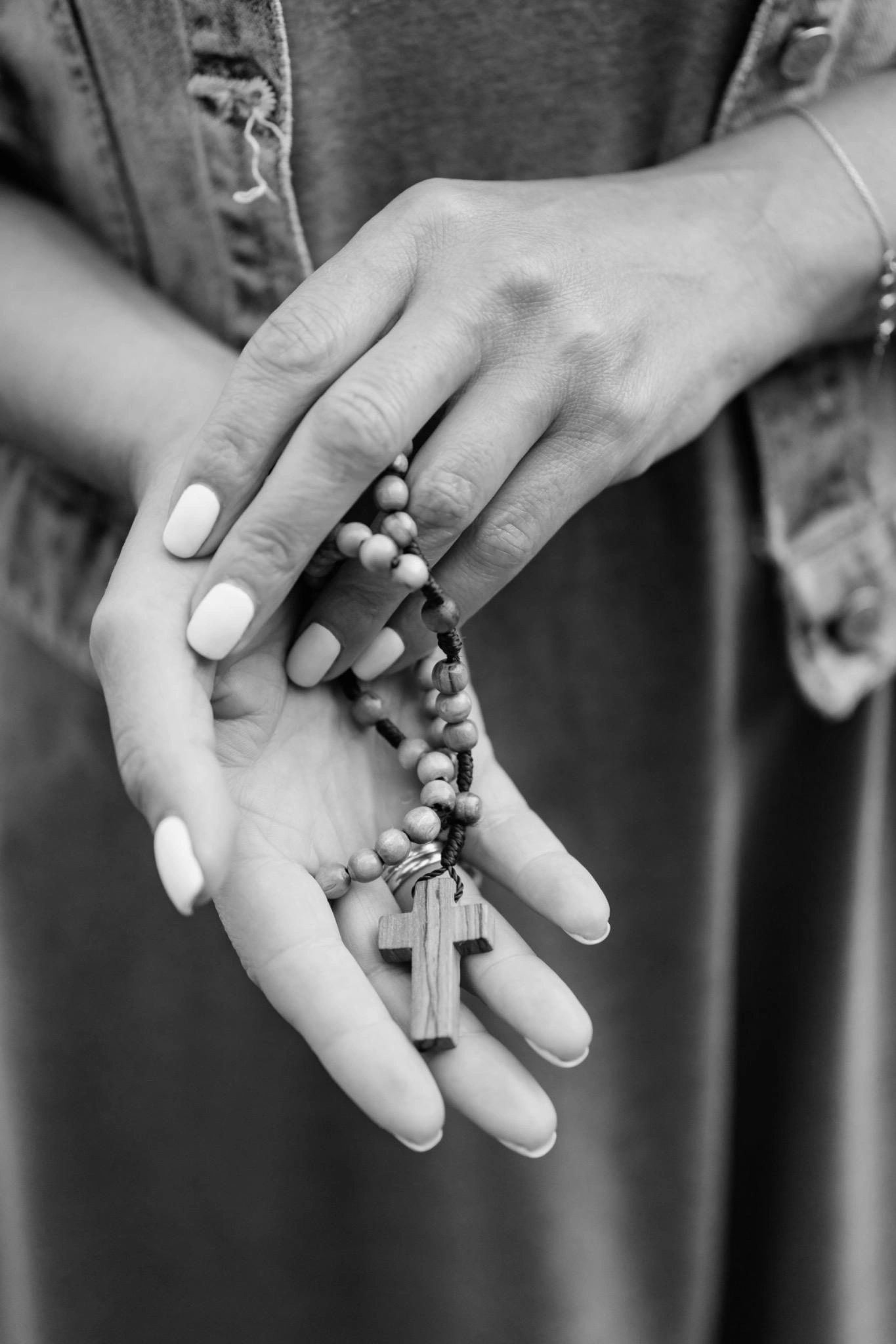 Hands holding a wooden cross rosary beads.