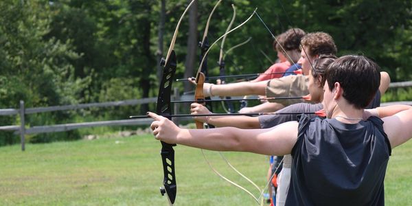 A group of young people practicing archery outdoors in a line.