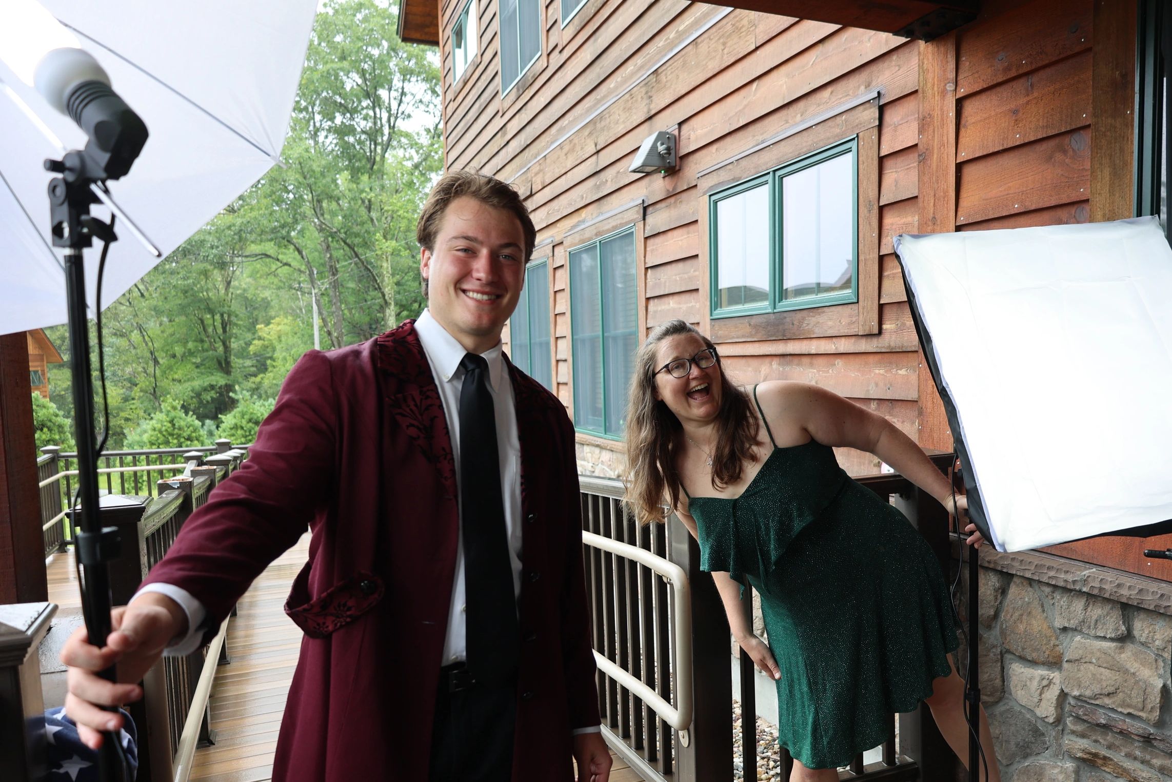 Two people smiling near lighting equipment on a wooden porch.