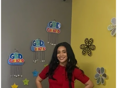 Young woman smiling in front of a colorful wall with motivational decorations.
