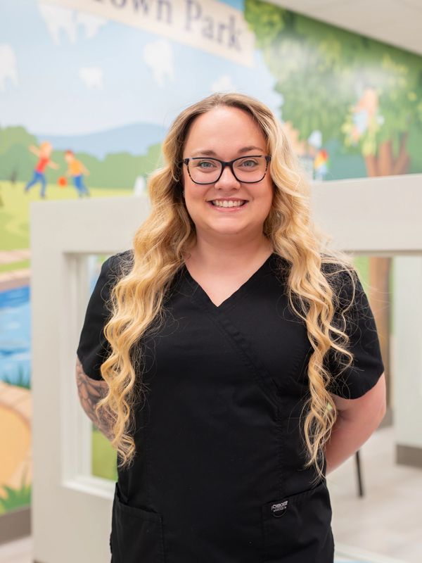 Smiling woman with long blonde hair and glasses in black scrubs.