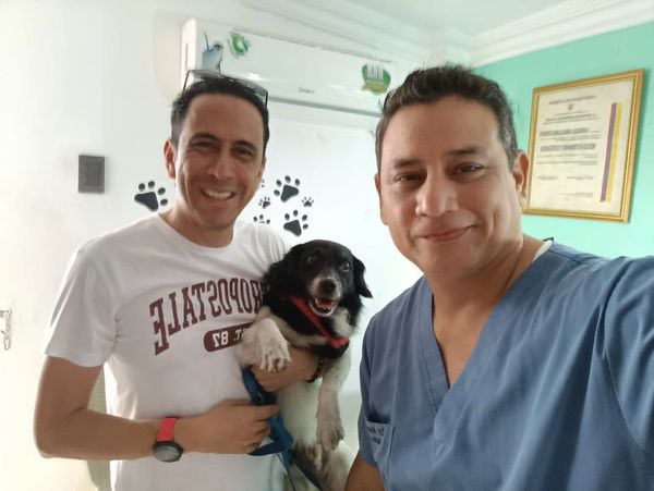 Two men smiling holding a small black and white dog indoors.