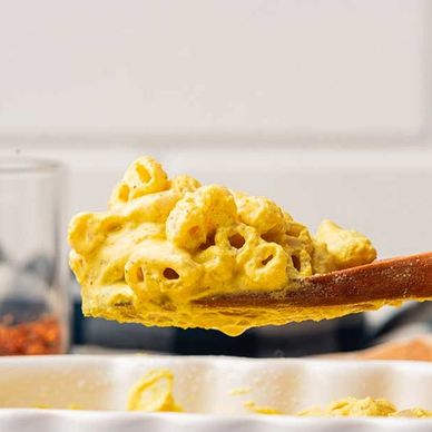 Wooden spoon scooping creamy macaroni and cheese from a white dish.