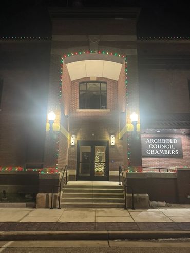 Entrance of Archbold Council Chambers decorated with Christmas lights and tree at night.