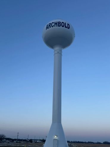 Tall white water tower with 'ARCHBOLD' written on it against a clear sky.