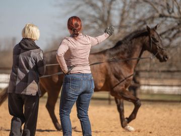 Two women training a horse in an outdoor arena.