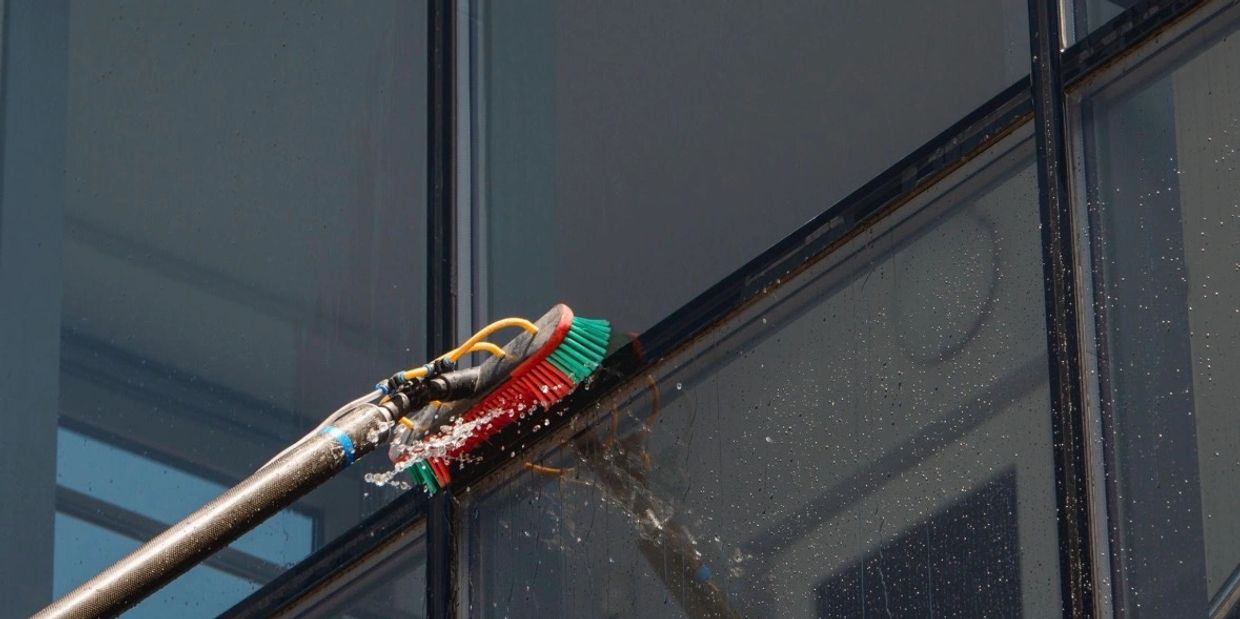 A brush with water sprays cleaning a glass window.