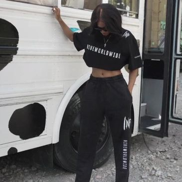 Woman in black tracksuit standing by vehicle.