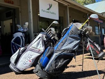 Golf bags filled with clubs standing outside a golf shop.