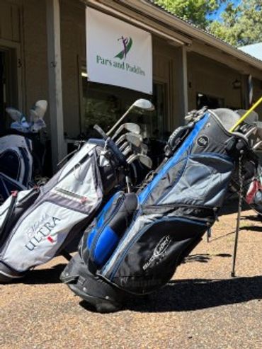 Golf bags filled with clubs standing outside a sports shop called Pars and Paddles.