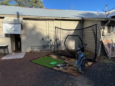 Outdoor golf practice setup with net and clubs beside a building.